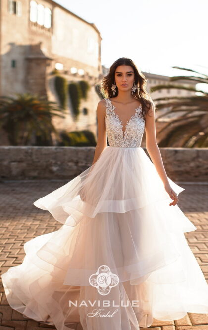 JANELLE 17327 - Naviblue JANELLE 17327 1 Naviblue Современное свадебное платье сочетает одном платье и модную иллюзию прозрачности и игривую пышность в виде воланов, которая в каждом сезоне привлекает смелых современных невест. Юбка в платье многослойная и объемная полностью покрыта оборками по всей длине, верх платья с V-образным вырезом, оформленным цветочным кружевом, делает акцент на тонкую шею и грациозные плечи невесты.