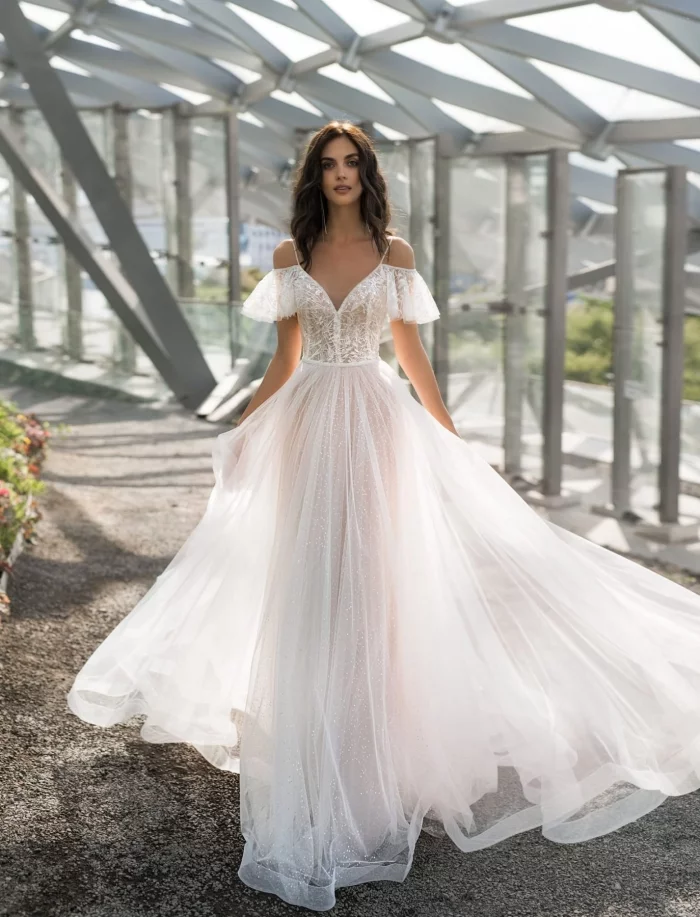 Melari 1 Наталья Романова Необычайно романтичное свадебное платье выполнено из нежного тюльмарина с блестящим эффектом. В этом красивом платье и многослойная пышная юбка, и кружевные рукавчики-крылышки и минимальный декор. Свадебное платье для невероятно стильной девушки!