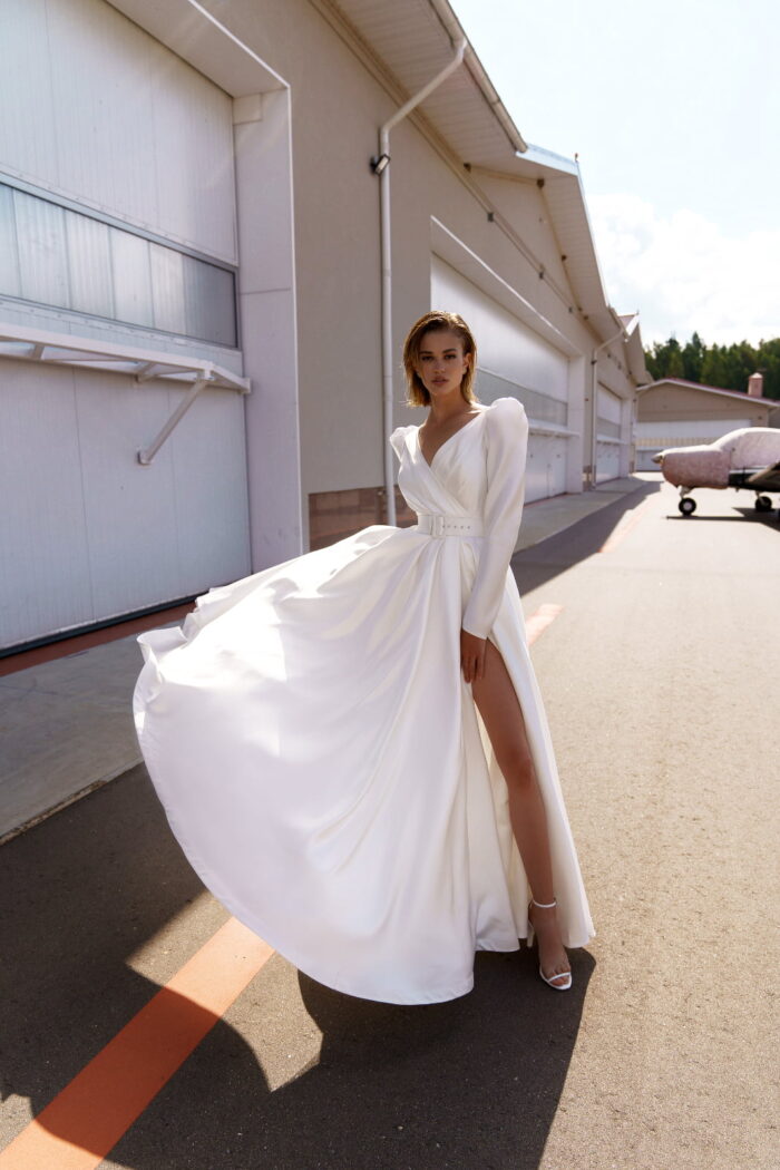 Lisbeth 5 Наталья Романова Свадебное платье с разрезом на юбке, с рукавами «жиго» и дизайнерским вырезом на спинке. Минималистичность кроя подчеркивает форму и элегантность платья.  Талия акцентирована широким поясом с прямоугольной пряжкой.