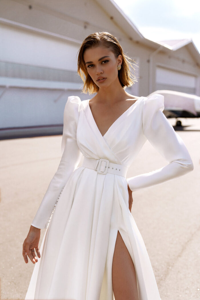 Lisbeth 3 Наталья Романова Свадебное платье с разрезом на юбке, с рукавами «жиго» и дизайнерским вырезом на спинке. Минималистичность кроя подчеркивает форму и элегантность платья.  Талия акцентирована широким поясом с прямоугольной пряжкой.