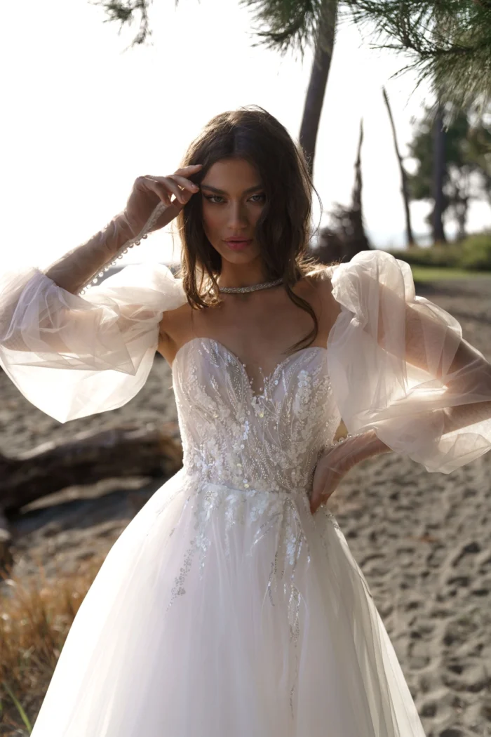 Лотти 3 Наталья Романова Любовь витает в воздухе, и это роскошное свадебное платье подходит для принцессы. Изысканное платье А-силуэта из струящегося тюля и кружева с эффектным V-образным вырезом и многочисленными многослойными оборками на юбке имеет тонкий лиф с длинными съемными рукавами. Спина на внутреннем корсете отделана кружевными аппликациями, которые создают поразительный силуэт.