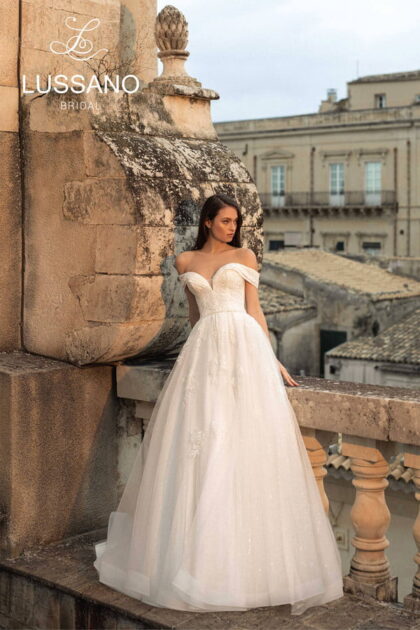 Rosemary 21042 - Lussano Rosemary 21042 1 Lussano Свадебное платье силуэта принцесса с мерцающей юбкой и утонченным декором. Корсет со шнуровкой на спине и вырезом «сердечко» дополняют спущенные бретели, открывающие плечи. Верх платья декорирован кружевными аппликациями, а талия акцентирована тонким поясом. Многослойная пышная юбка выполнена из фатина, покрытого мелкими переливающимися блестками.