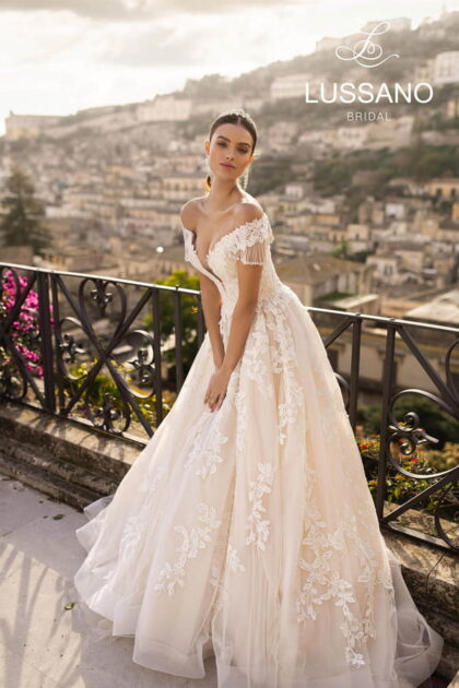 Ria 19400 - Lussano Ria 19400 1 Lussano Пышное свадебное платье, украшенное белым кружевом. Корсет на шнуровке с кружевными узорами. Юбка со шлейфом выполнена из многослойного фатина.