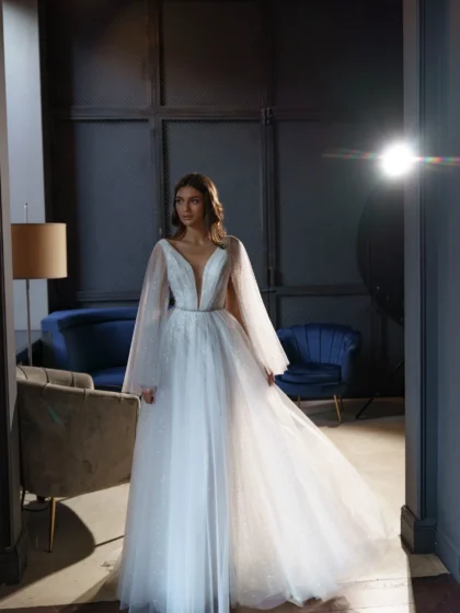 Ева - Сониа Солей Ева 1 Сониа Солей <p style="text-align: justify;">Свадебное платье Ева А-силуэта - это идеальный выбор для невест, которые хотят выглядеть элегантно и впечатляюще в свой важный день. Это платье имеет V-образный вырез, который подчеркивает красоту шеи и груди, придавая образу нежности и женственности. Но самым впечатляющим элементом этого платья являются объемные крылья на плечиках, которые создают эффектное и роскошное ощущение. Они придают платью небесный и легкий вид, как будто невеста летит под венец. Спинка платья застегивается на молнии, что обеспечивает удобное и легкое надевание. Это позволяет невесте чувствовать комфорт на протяжении всего свадебного мероприятия. Основной материал, используемый в этом платье, - это фатин. Фатин - легкая, но одновременно элегантная ткань, которая создает воздушное и романтичное ощущение. В сочетании с глиттером, этот материал придает платью блеск и сияние, подчеркивая изысканность и роскошь внешнего вида. Свадебное платье Ева А-силуэта с V-образным вырезом и объемными крыльями на плечах является уникальным и неповторимым выбором для невесты, которая хочет быть обрамленной грацией и роскошью в свой великий день.</p>
<iframe src="https://www.youtube.com/embed/_WmakzHHiM0" width="auto" height="600" frameborder="0" allowfullscreen="allowfullscreen"></iframe>