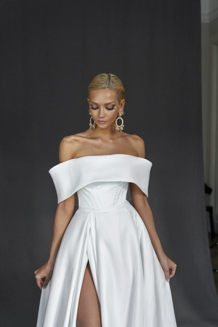 Розмари 1 Martha (Марта) Это стильное свадебное платье А-силуэта, выполненное из элегантного крепа, воплощает в себе утонченность и женственность. Открытый верх платья подчеркивает декольте и плечи, создавая романтичный и притягательный образ. Юбка платья плавно расширяется от талии, формируя изящный А-силуэт. Разрез в юбке не только добавляет нотку смелости и современности, но и обеспечивает комфорт и свободу движений, позволяя невесте уверенно шагать и танцевать. Спинка на молнии гарантирует идеальную посадку, а креп, обладая хорошей драпировкой, создает эффектный силуэт, который подчеркивает каждый изгиб фигуры. Это платье станет идеальным выбором для невесты, желающей сочетать элегантность и динамичность, подчеркнув свою индивидуальность и стиль