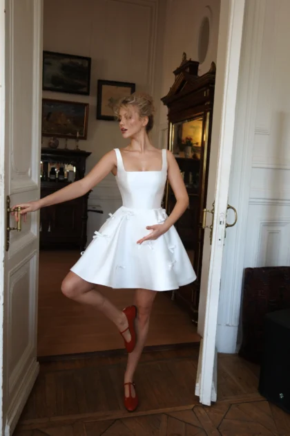 Чатни 1 Наталья Романова <p style="text-align: justify;">Короткое свадебное платье с квадратным вырезом на бретелях — это игривый и свежий выбор для невесты, стремящейся добавить нотку романтики и легкости в свой образ. Этот стиль идеально подходит для менее формальных свадеб или уникальных атмосферных торжеств, а также для свадебных вечеринок.
Квадратный вырез подчеркивает декольте, акцентируя внимание на шее и плечах, в то время как бретели добавляют дополнительный комфорт и поддержку. Декоративные бантики на юбке придают платью игривость и занимательность, создавая объем и подчеркивая женственность.
Основной материал — микадо — обеспечивает наряду структуру и изысканный внешний вид. Он сочетает в себе легкость и прочность, что позволяет платью держать форму и быть удобным в носке. Это короткое свадебное платье станет отличным выбором для стильной невесты, стремящейся выделиться среди традиционных свадебных образов.
Модель доступна в размере плюс сайз.</p>
