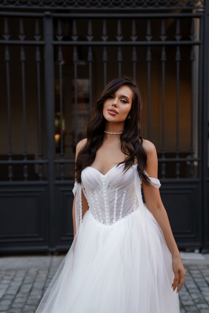 Оберон - Сонеста Оберон 1 Сонеста <p style="text-align: justify;">Свадебное платье А-силуэта с драпированным корсетом и жемчужинами — это наряд, который сочетает в себе романтичность и элегантность. А-силуэт имеет утонченную форму, которая подходит многим типам фигур, плавно очерчивая линии тела и создавая эффект легкости.
Драпированный корсет украшен жемчужинами, что добавляет платью роскоши и блеска. Драпировка создает красивые складки, подчеркивающие линию талии и придающие образу текстурное разнообразие. Жемчужины добавляют яркости и изысканности, превращая ткань в настоящий фокус внимания.
Основной материал — фатин, известный своей воздушностью и легкостью, создает ощущение романтики и невесомости. Он придает платью объем и структуру, позволяя юбке красиво ложиться и драпироваться.
Сотуар для шеи, предлагаемый в комплекте (продается отдельно), станет отличным дополнением к образу и поможет подчеркнуть красоту neckline. Это украшение поможет создать завершенный вид, добавляя нотку шикарности и утонченности.</p>
<iframe src="https://www.youtube.com/embed/-qiz6TV5XJs" width="auto" height="600" frameborder="0" allowfullscreen="allowfullscreen"></iframe>