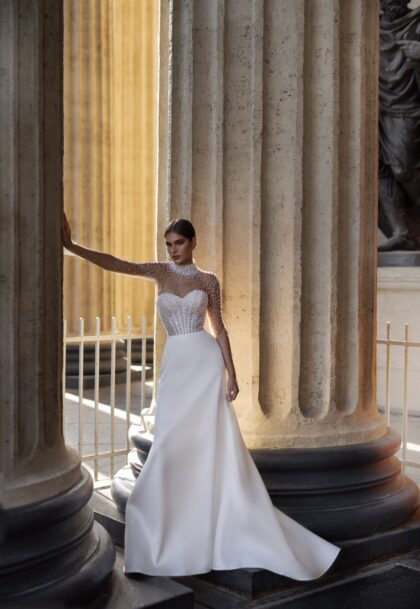 Дора 1 Патрисия Кутюр <p style="text-align: justify;">Дополненное расшитым жемчугом боди с длинными рукавами, платье создает эффектный и стильный силуэт, который отлично подходит для невест, предпочитающих более классический и романтичный стиль. Пышная юбка придаёт образу объём и легкость, а декоративный бант добавляет нотку игривости и оригинальности.
Основной материал микадо обеспечивает не только шикарный внешний вид, но и комфорт в носке. Это платье идеально подойдет для торжественной и запоминающейся свадьбы, представляя собой великолепный баланс между традициями и современными тенденциями.</p>
<iframe src="https://www.youtube.com/embed/G7xB1fQ8z3E" width="auto" height="600" frameborder="0" allowfullscreen="allowfullscreen"></iframe>