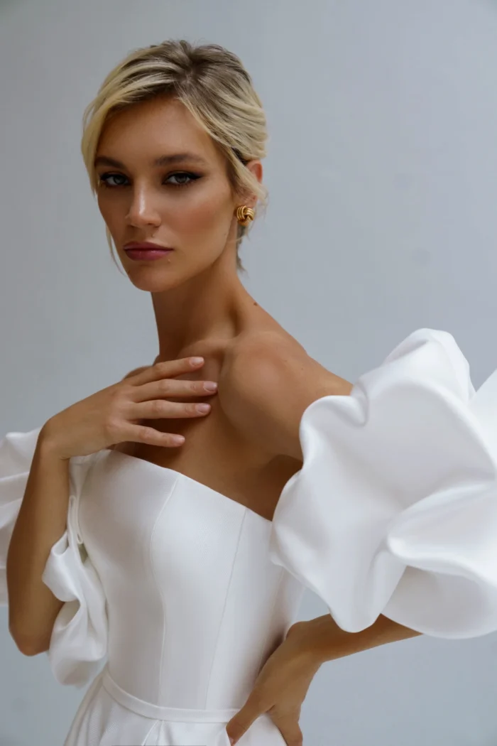 Калипсо 1 Наталья Романова <p style="text-align: justify;">Свадебное платье А-силуэта из атласа с разрезом на юбке и спинкой на молнии идеально сочетает элегантность и современность. Объемные рукава добавляют романтический шарм, подчеркивая изящность силуэта.</p>
