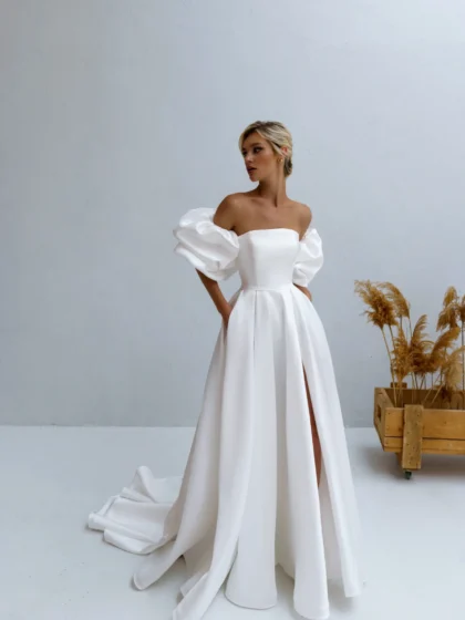 Калипсо 1 Наталья Романова <p style="text-align: justify;">Свадебное платье А-силуэта из атласа с разрезом на юбке и спинкой на молнии идеально сочетает элегантность и современность. Объемные рукава добавляют романтический шарм, подчеркивая изящность силуэта.</p>
