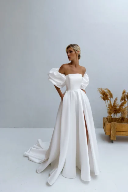 Калипсо 1 Наталья Романова <p style="text-align: justify;">Свадебное платье А-силуэта из атласа с разрезом на юбке и спинкой на молнии идеально сочетает элегантность и современность. Объемные рукава добавляют романтический шарм, подчеркивая изящность силуэта.</p>
